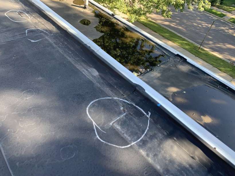 Chalk circle marking a suspected hail hit beside the metal edge of the rubber flat roof at Washington Place in St. Cloud, MN