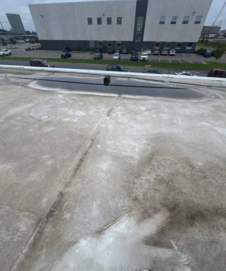 Worn membrane and a dark ponding ring near the parapet on the old Bloomington Lincoln flat roof in Bloomington, July 2024