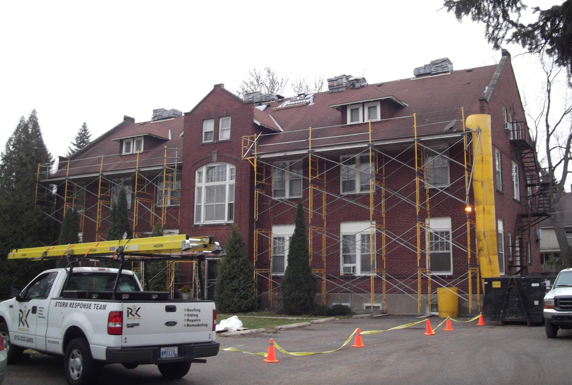 Historic brick multi-family building with scaffolding during a Repair King roof tear-off, Storm Response Team truck in front