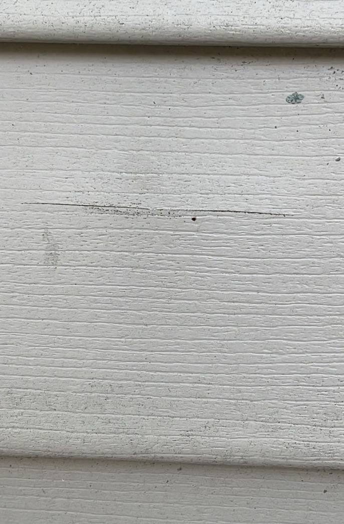 Close-up of a small crack and impact marks in tan vinyl siding on a Lake Elmo manufactured home, July 2023