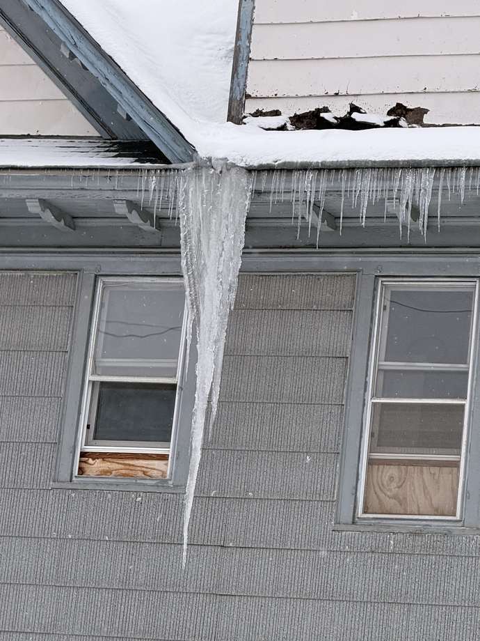 Massive icicle hanging from an eave next to torn and damaged roofing above