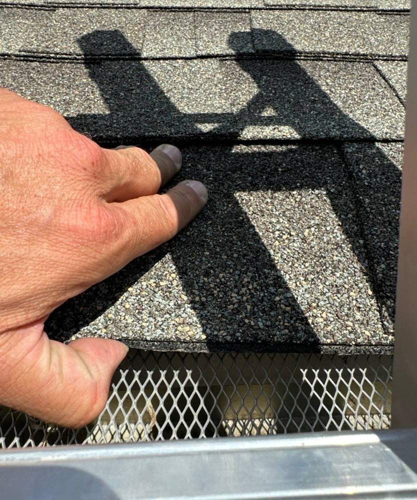 Lifting a ridge cap shingle to check the underlayment during a Maple Grove roof inspection, September 2022