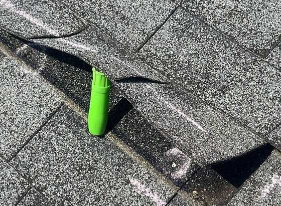 Shingle tab lifted during a seal check, showing a torn tab and chalk marks on a Woodbury roof, June 2023