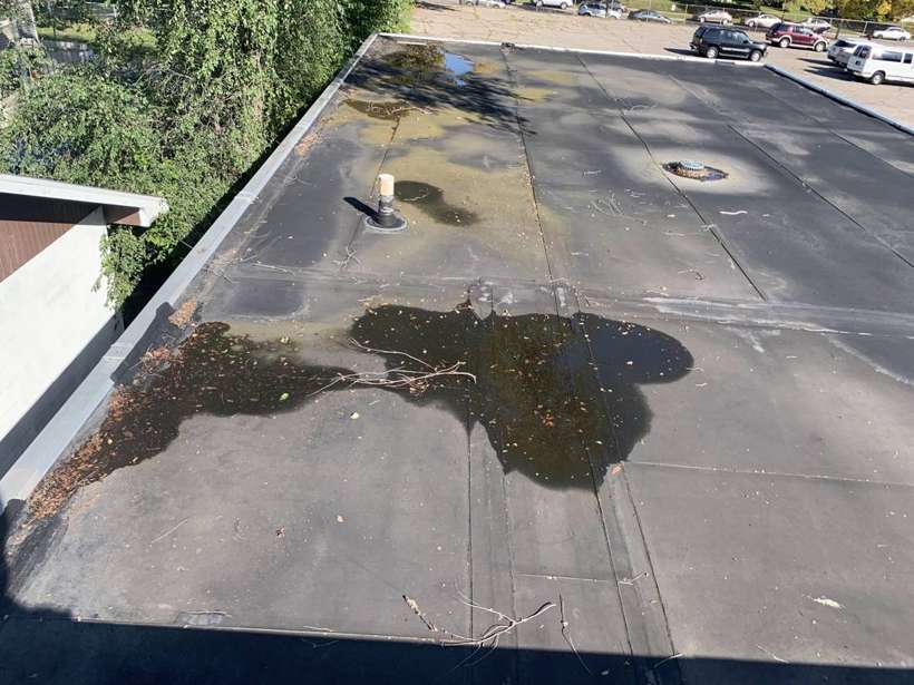Standing water and debris on the black rubber flat roof at Washington Place in St. Cloud, MN, during a Repair King inspection