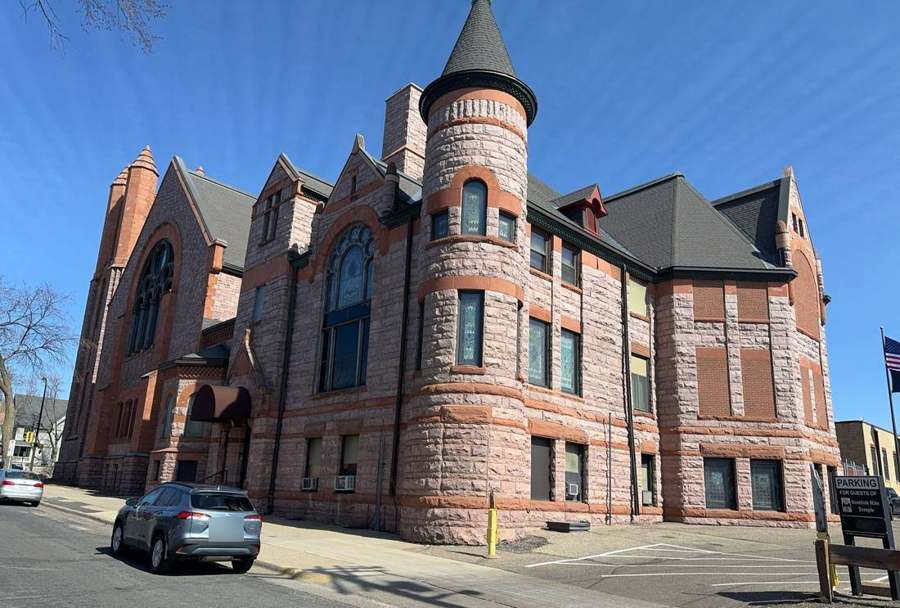 Pink sandstone Scottish Rite Temple in Minneapolis with a conical turret and large stained-glass window, photographed during a Repair King inspection in March 2024