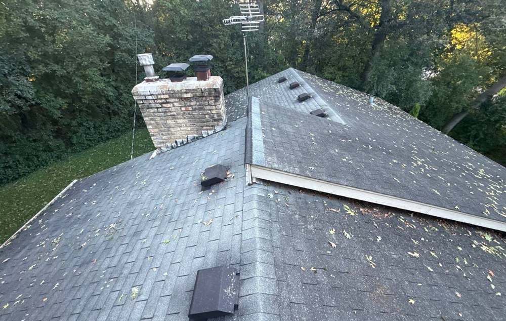 Asphalt shingle roof with a brick chimney surrounded by mature trees in Minnetonka, MN, inspected by Repair King in September 2025
