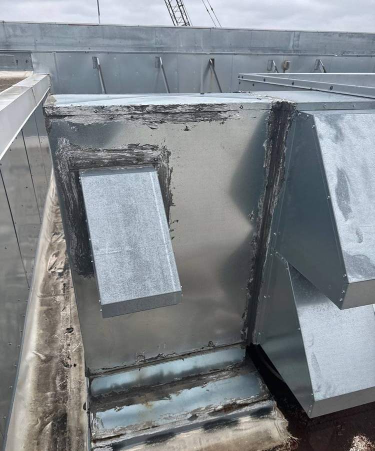 A rooftop unit curb with patched flashing beside the parapet on the Bloomington Lincoln roof, July 2024