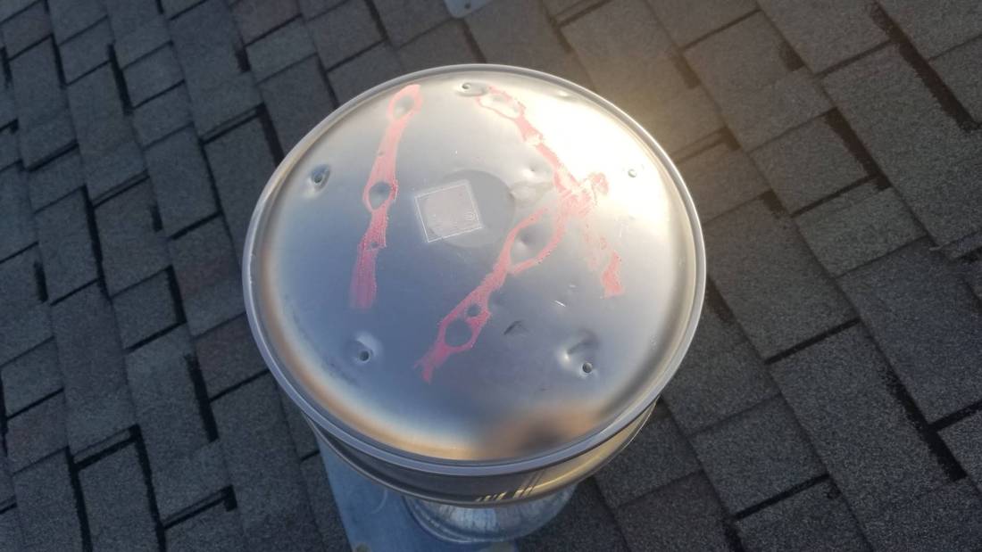 Dented round metal vent cap with chalk marks on the roof of Mega Coin Laundry in Fairmont, MN