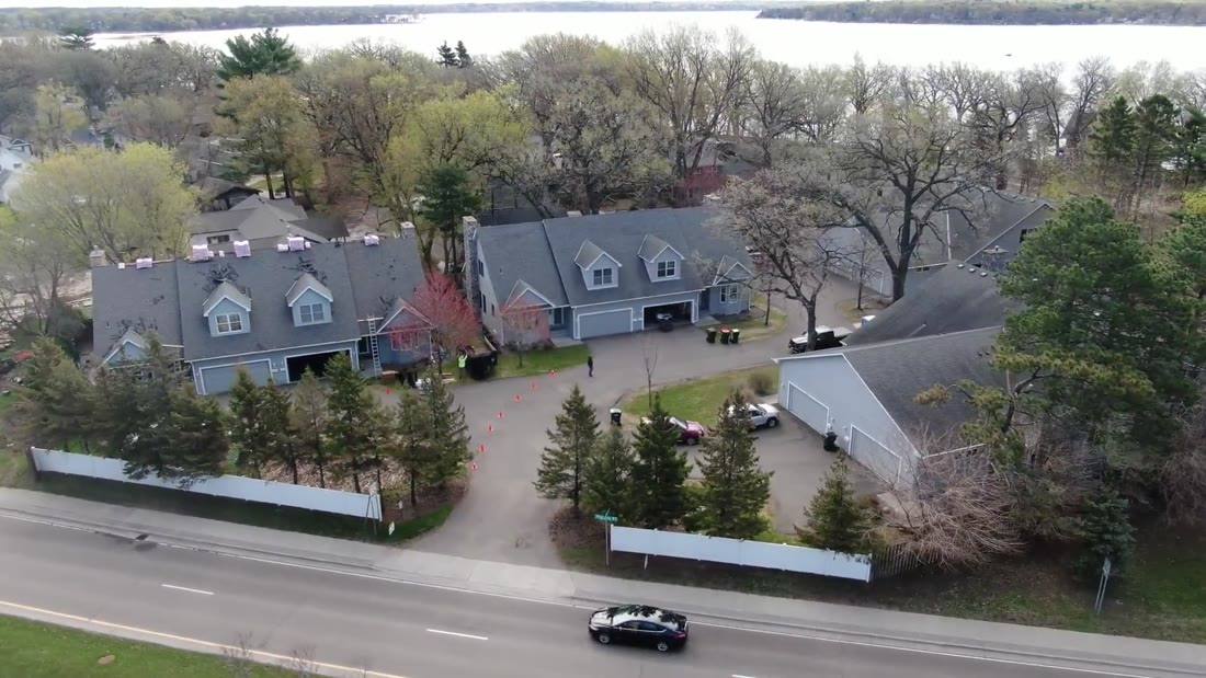 Drone view of gray townhome buildings with steep gables and dormers in White Bear Lake, MN, a Repair King multifamily roofing project, with White Bear Lake in the background