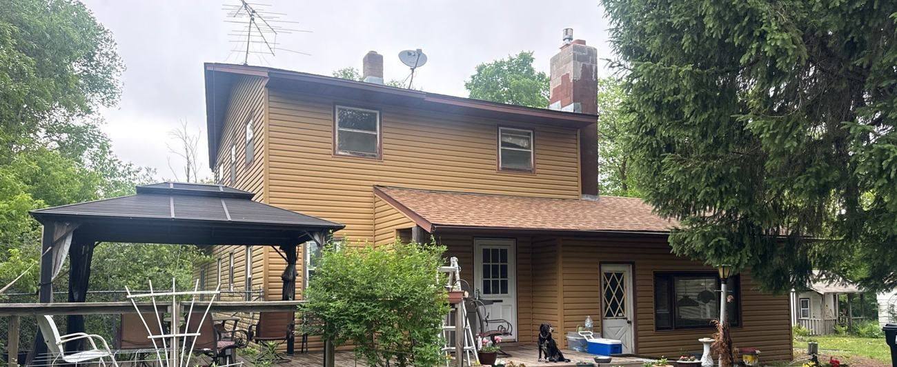 Two-story home with tan siding, a covered porch and gazebo on a wooded lot in Stacy, MN, photographed by Repair King during a June 2026 roof inspection