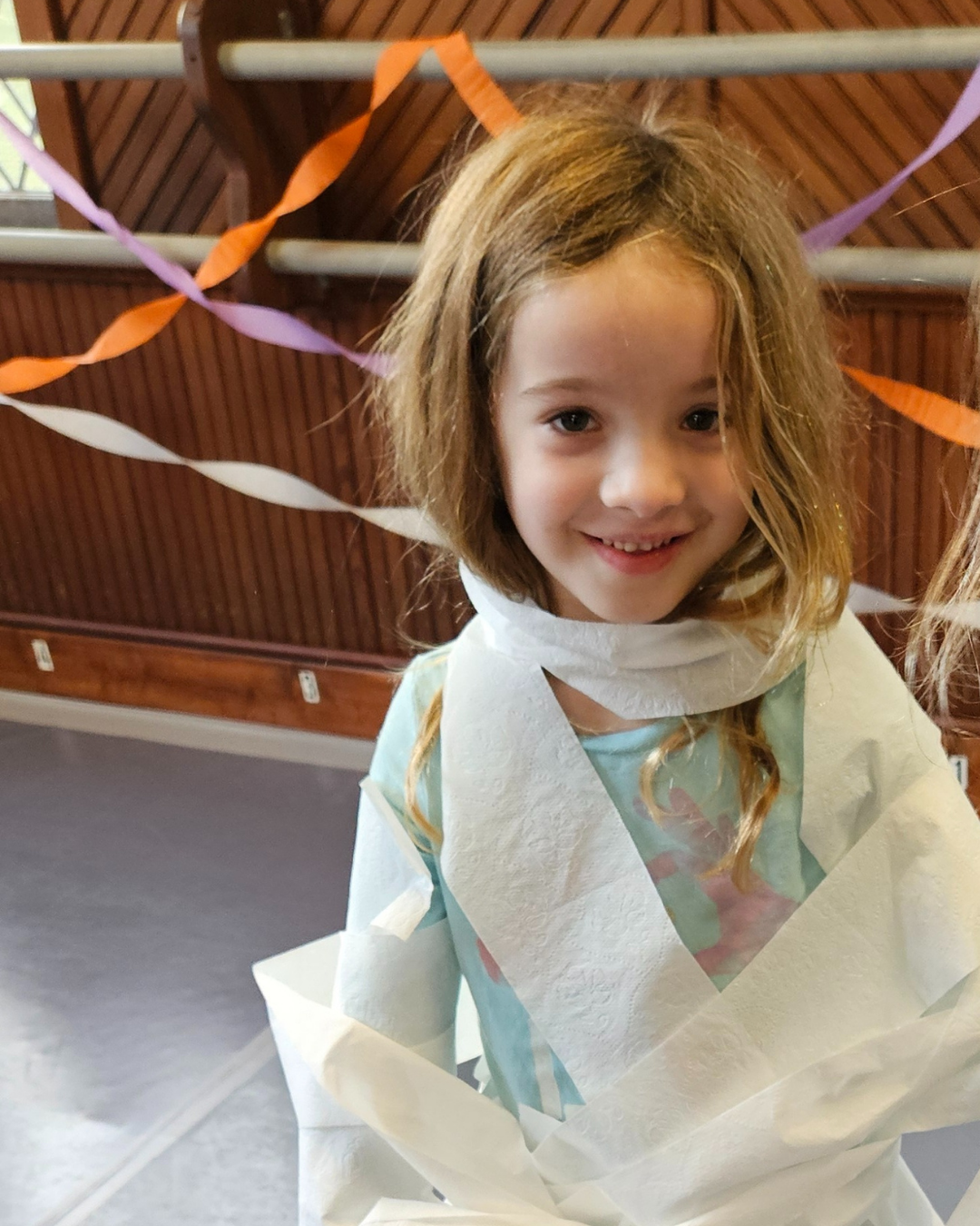 Smiling child wrapped like a mummy during a Halloween game at Boo Bash, Prince William Dance Academy, Nokesville, VA