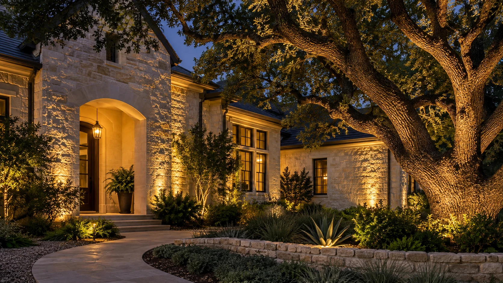 Illustrative uplighting concept with warm light on a mature tree, landscaping and textured stone exterior