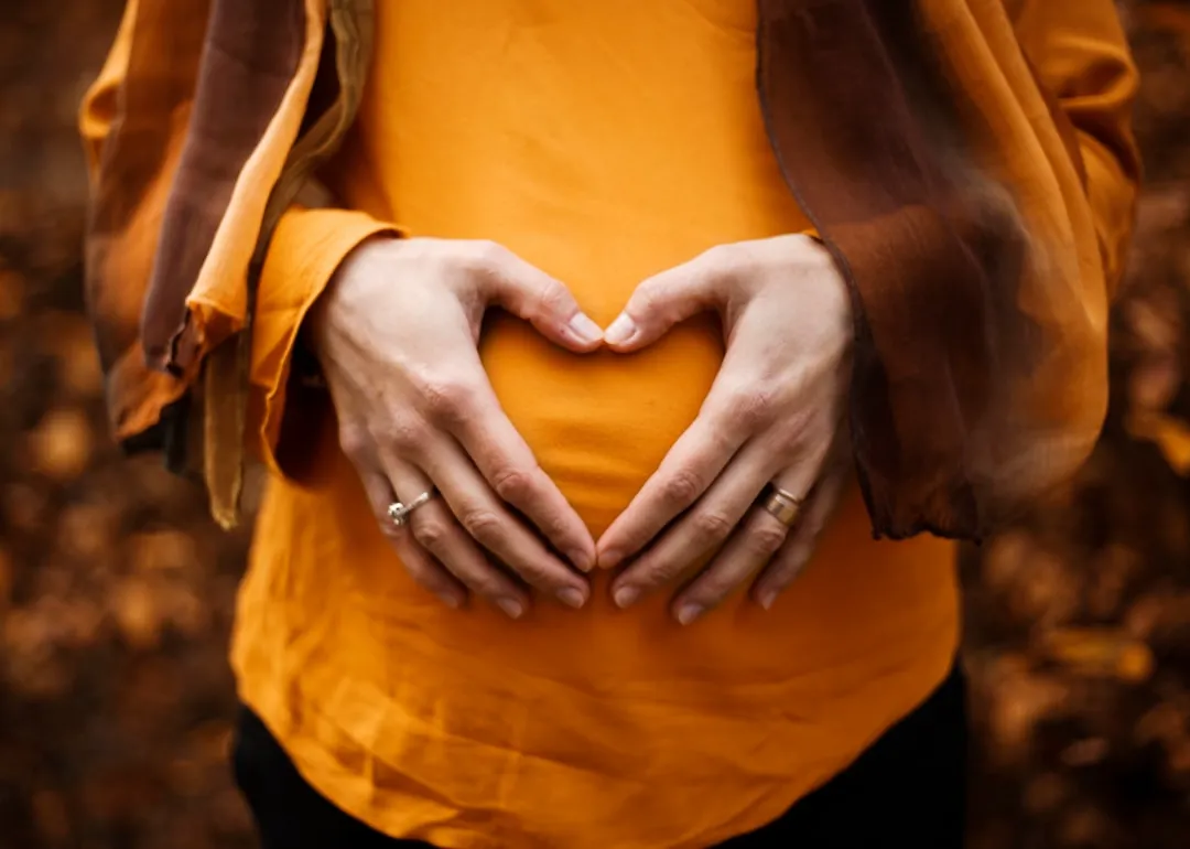 pregnant woman with her hands shaped like a heart over her baby bump