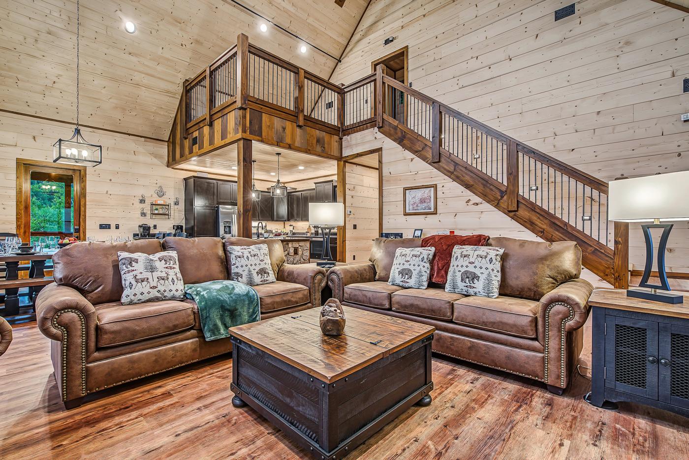 Living room — leather sofas, rustic trunk, loft, and staircase