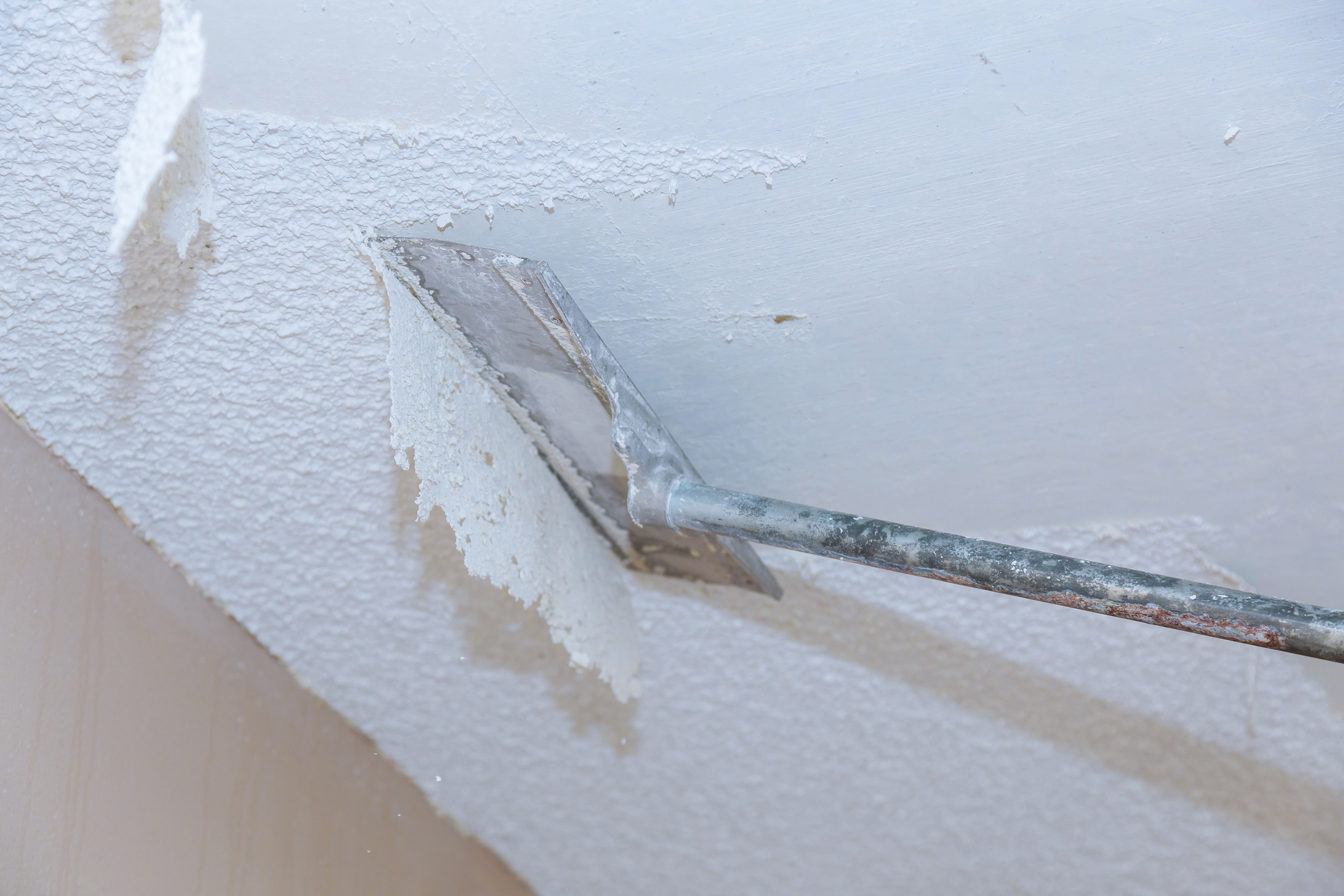 Popcorn ceiling texture removal using a flat scraping tool to lift dated texture and smooth the ceiling surface before painting