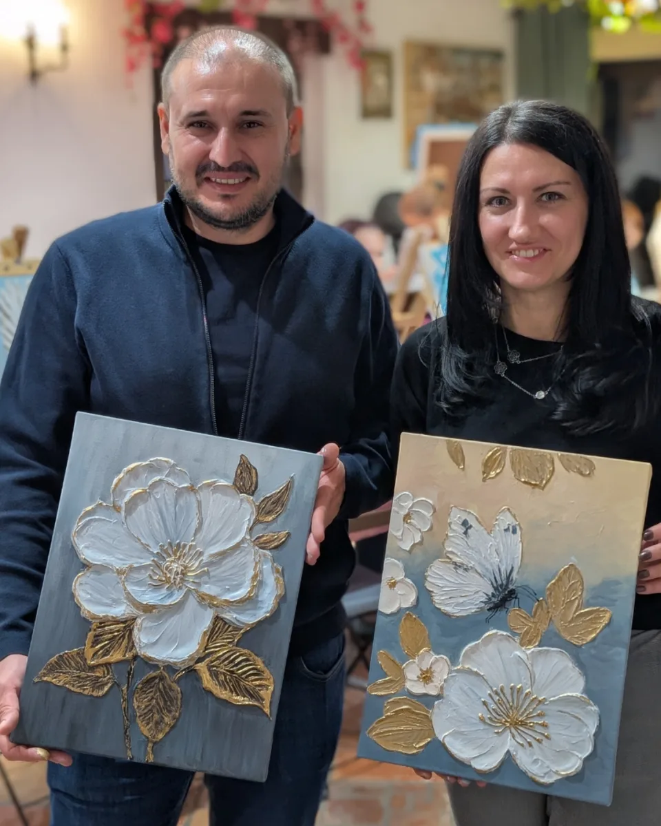 Un cursant și o cursantă de la atelierul de începători, fiecare cu tabloul lui în relief cu flori albe