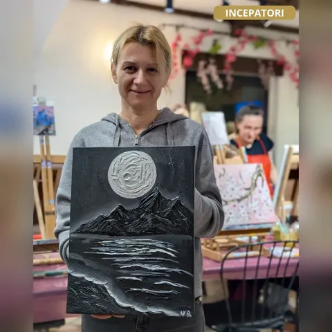 Cursantă de la atelierul de începători, cu tabloul ei în relief cu lună și munți