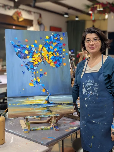 Gabriela G. la șevalet, lângă tabloul ei mare în relief cu un fluture albastru și auriu