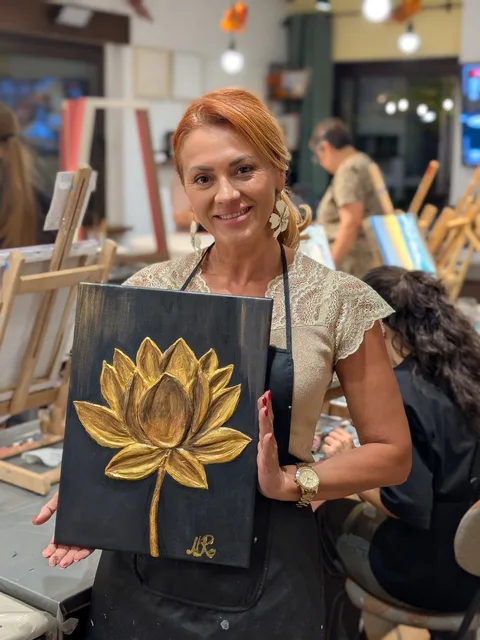 Cursantă zâmbitoare cu tabloul terminat, un lotus auriu în relief pe fond închis