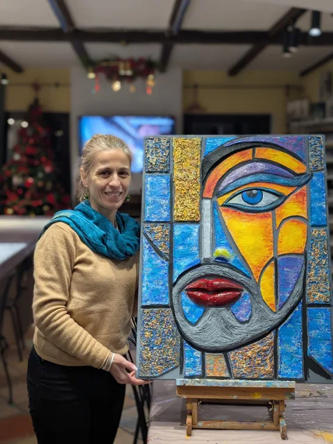 Cursantă din abonament lângă tabloul ei mare în relief, un chip de femeie în stil cubist, albastru și auriu