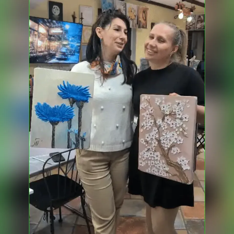 Două prietene zâmbitoare își arată tablourile în relief la finalul unei seri la Melinda Art