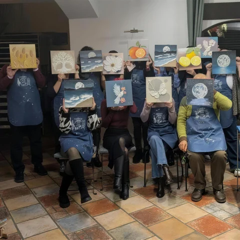 Echipă de colegi la un team building Melinda Art, care își țin tablourile în relief în fața feței