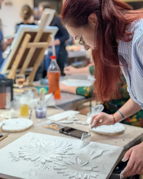 Cursantă modelând cu spatula florile din pastă albă pe pânză, la atelier