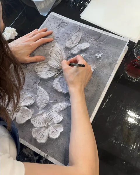 Cursantă desenând cu creionul conturul modelului pe pânză, peste formele de flori și fluturi