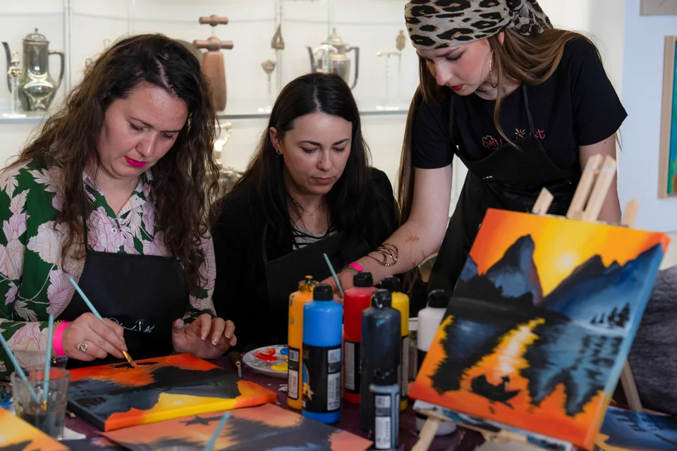 Instructoare Melinda Art care ghidează două colege la șevalet