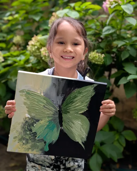 Fetiță zâmbitoare cu primul ei tablou în relief, un fluture verde