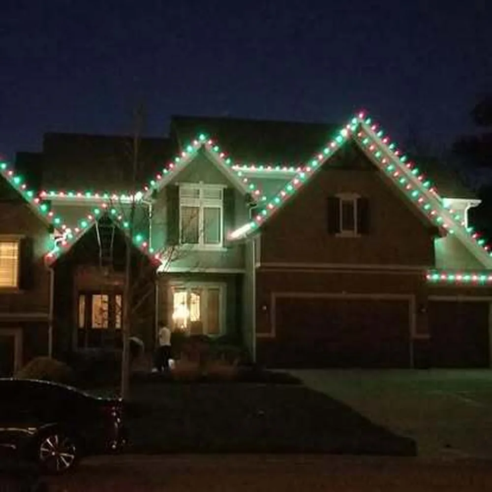 Green, red and white C9 bulbs on a two-story home with an extension ladder in place