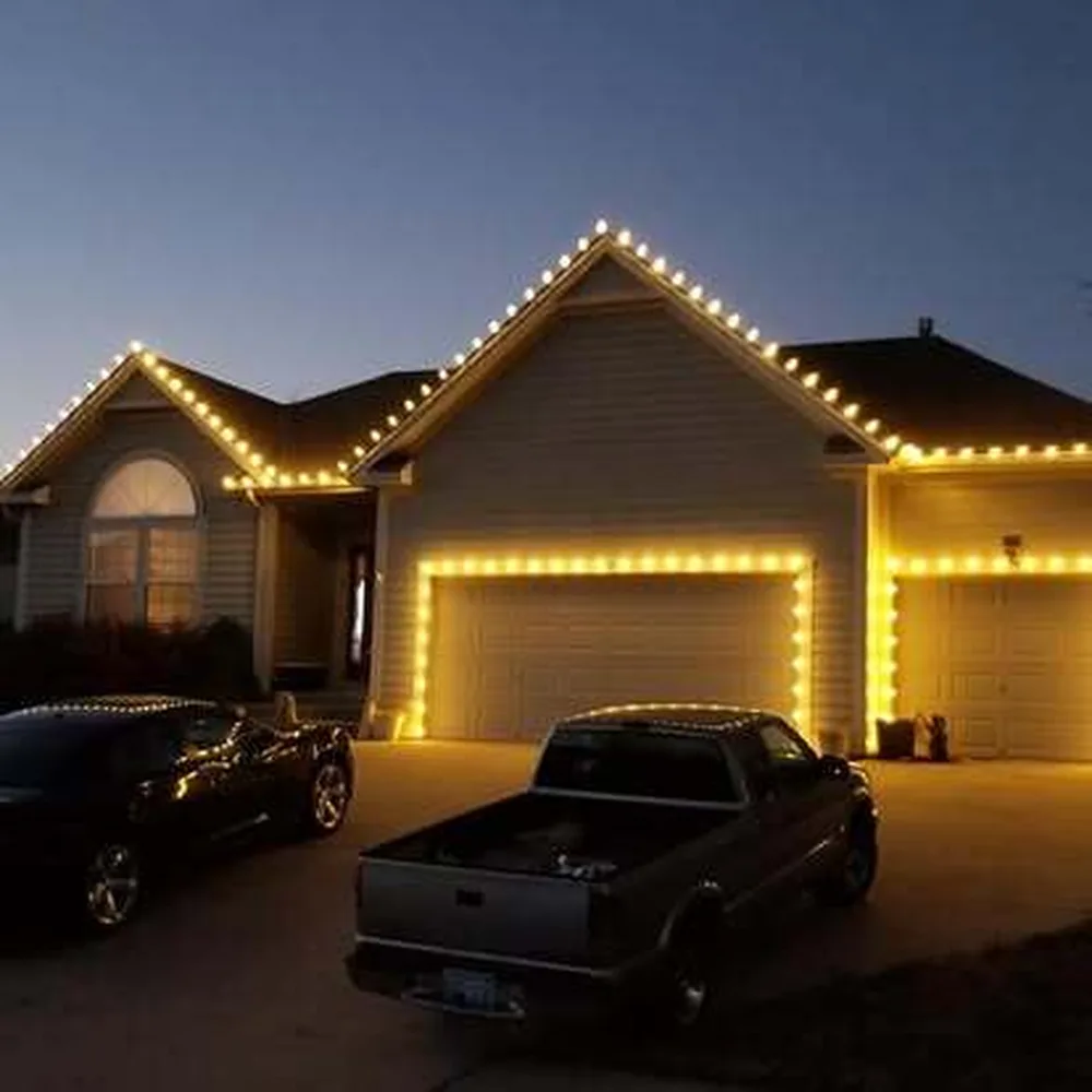 Warm white C9 bulbs on a tan two-story home with a truck and car in the driveway at dusk