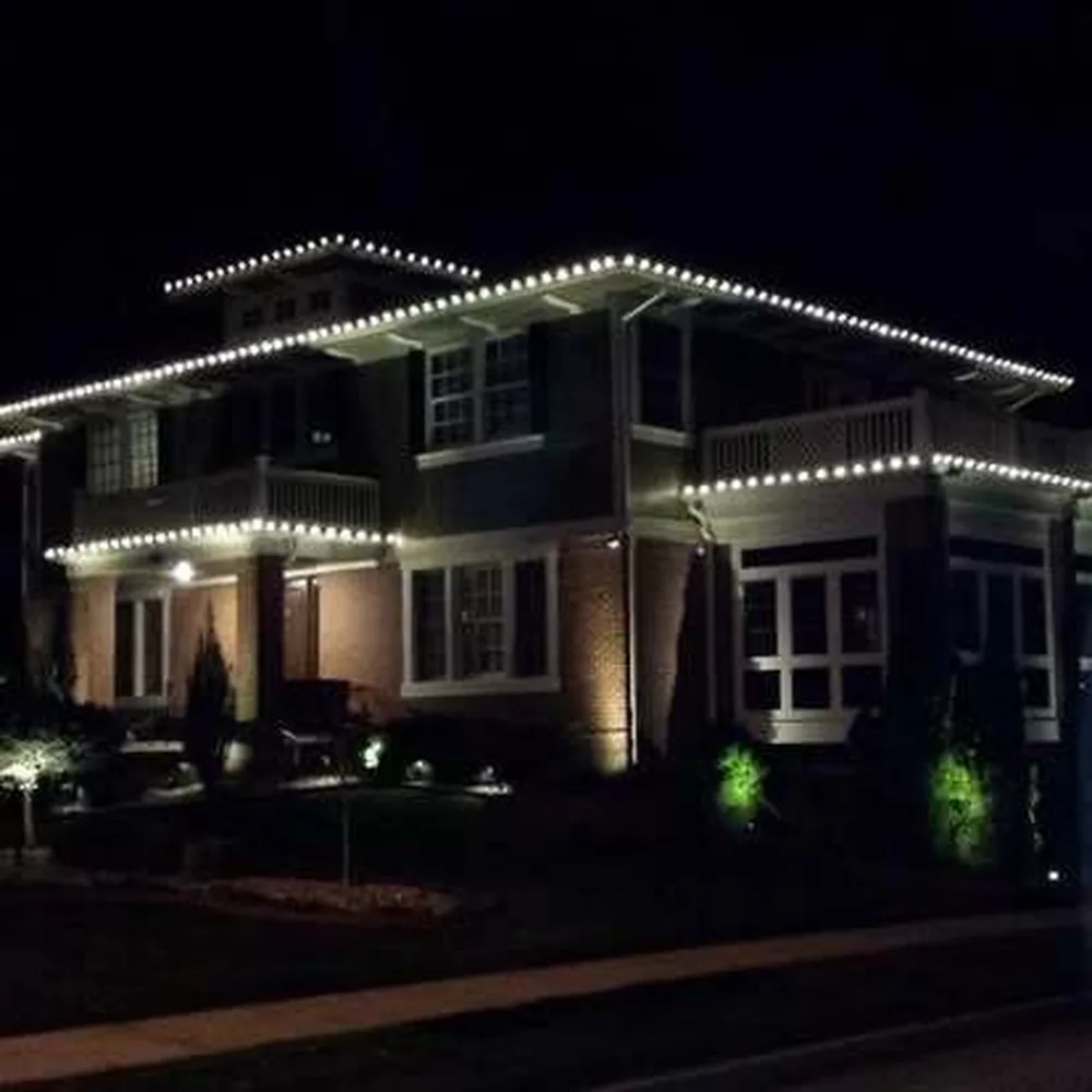 Warm white C9 bulbs along the roofline and balcony railings of a dark brick two-story home