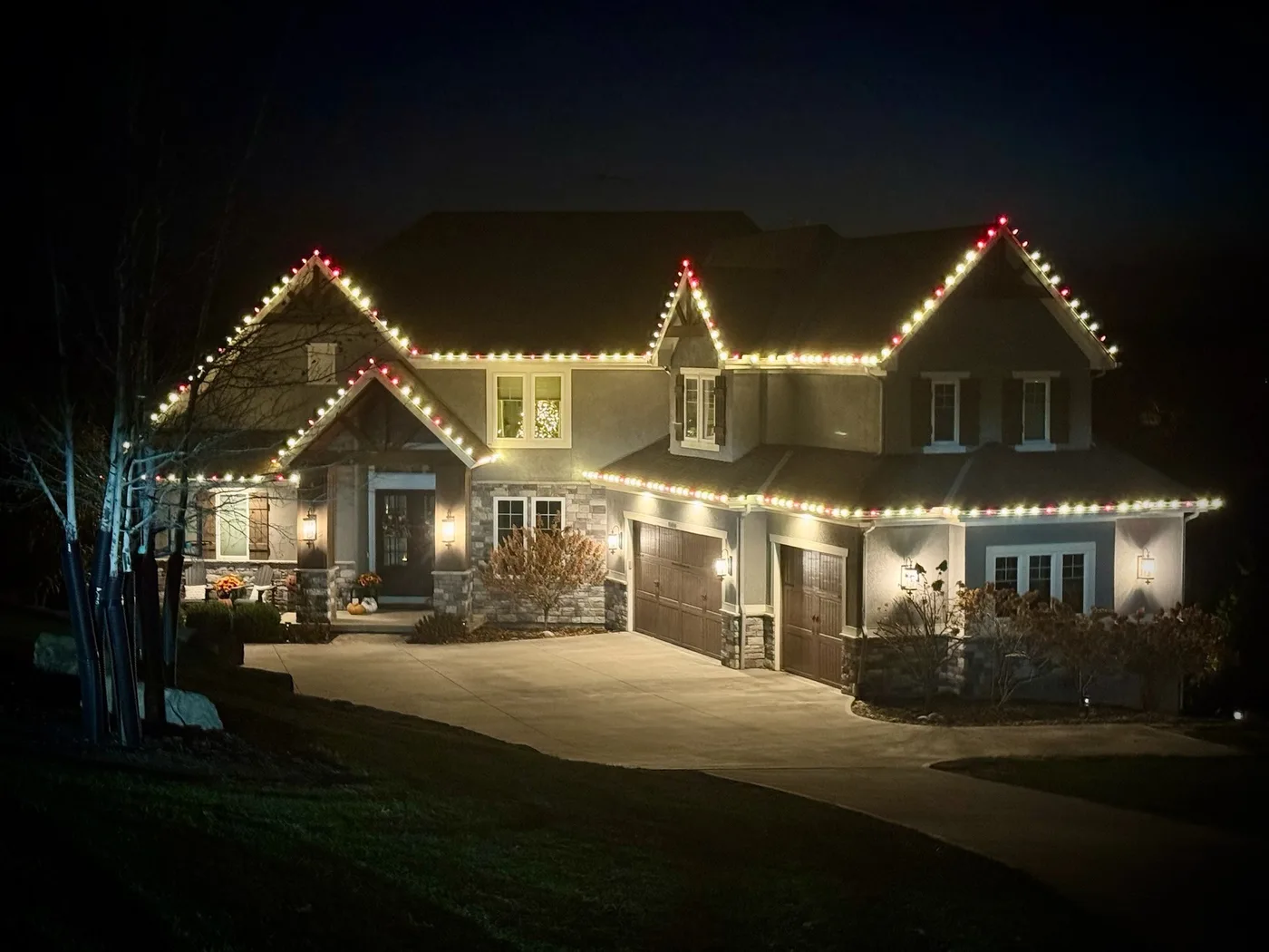 A stone and stucco two-story home outlined in warm white and red C9 Christmas lights at night