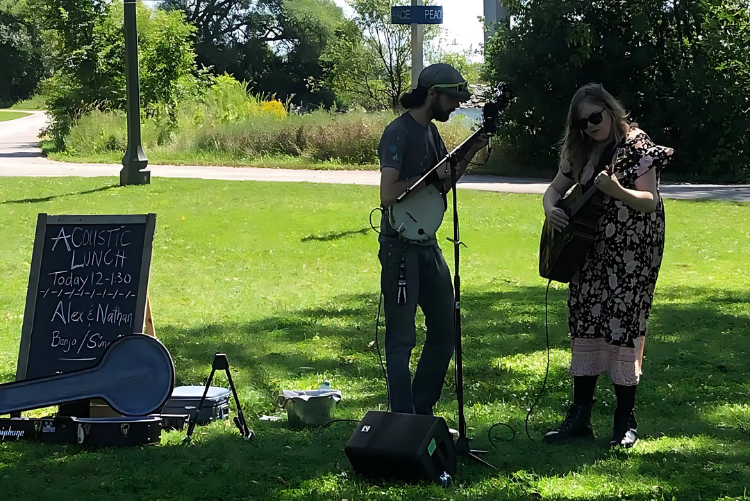 Alex and Naihan performing live acoustic music with banjo and guitar during Acoustic Lunch at Pop-Ups on the Bay in Belleville, Ontario.