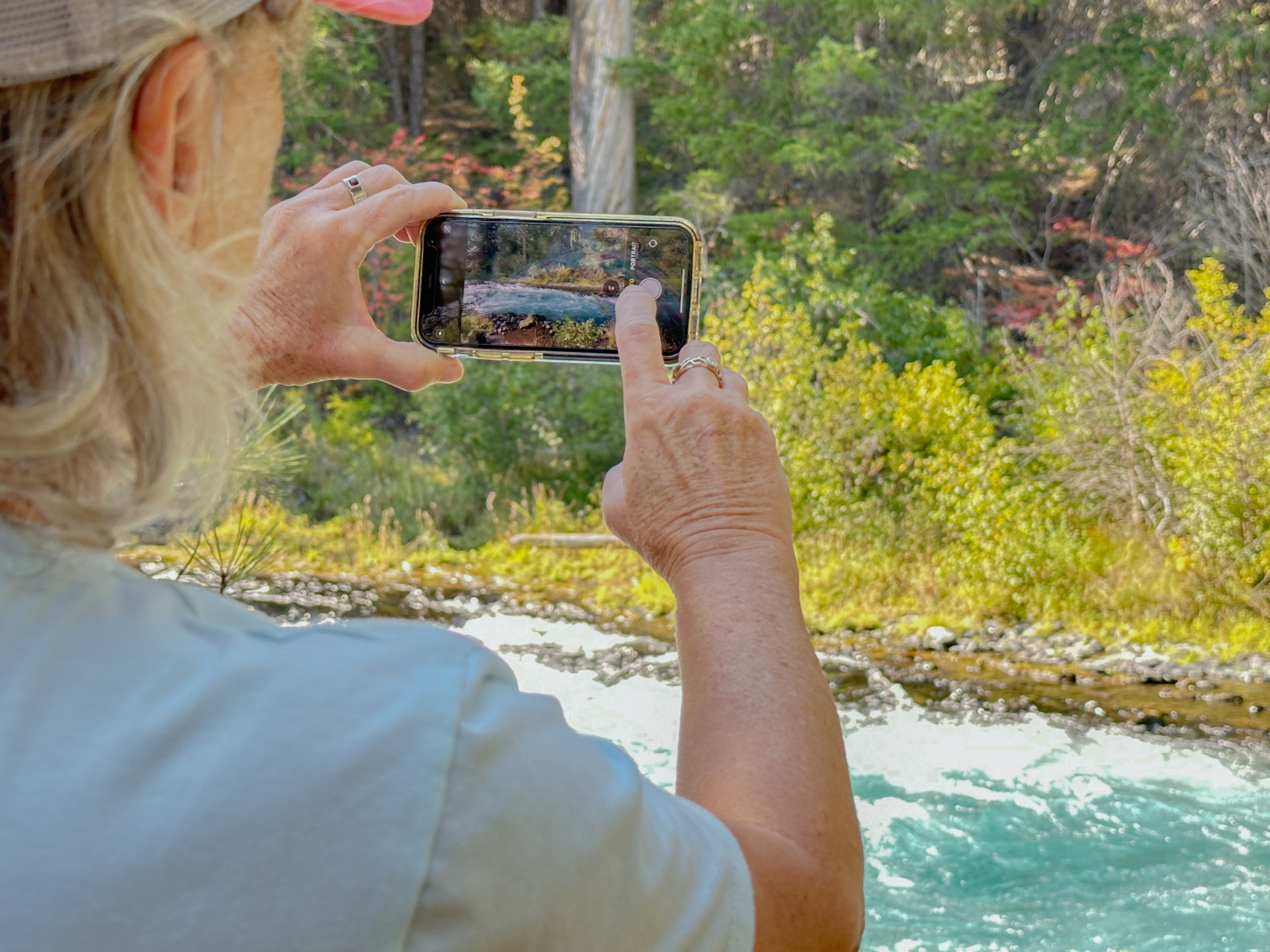 Woman using iPhone camera app outdoors at the Metolius River, Oregon