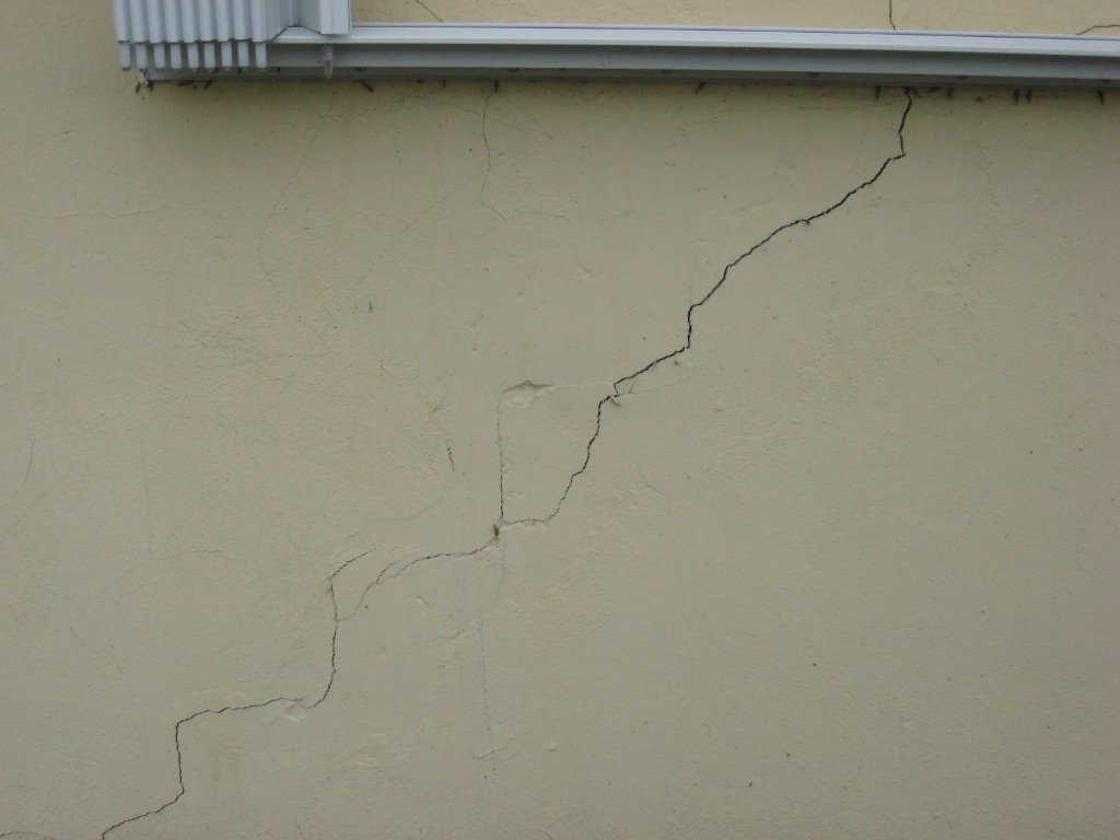 Stair-step crack running diagonally across an exterior stucco wall