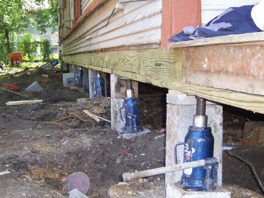A raised home supported on temporary jacks and blocking during foundation work