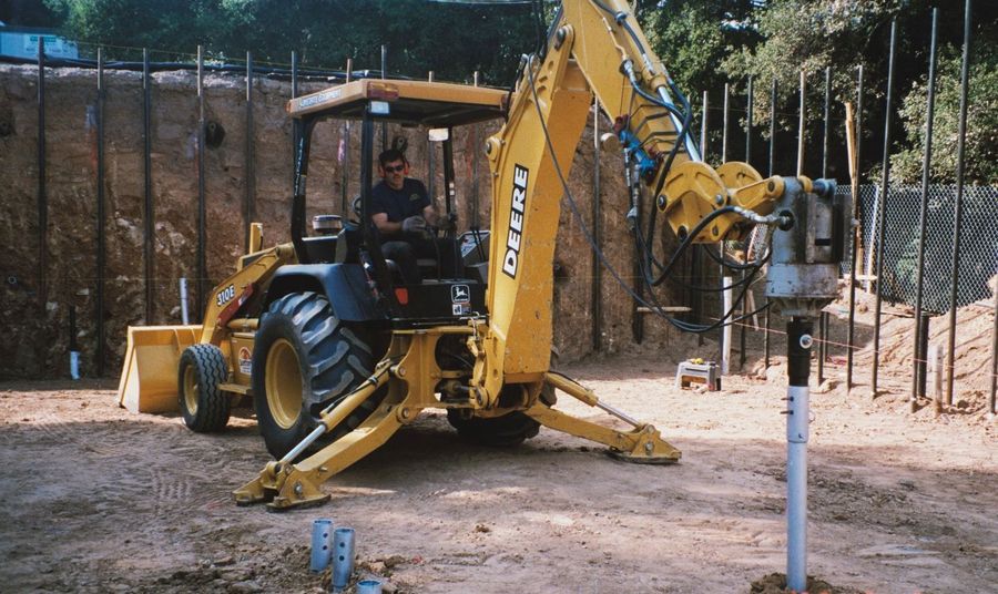 Drive head on a backhoe installing a helical pile beside a silt fence