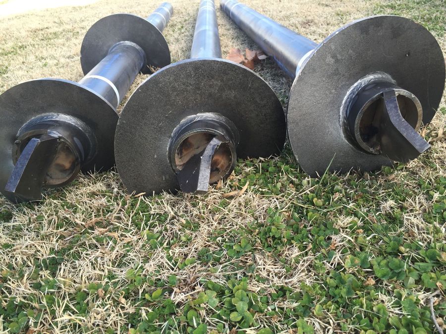 Close-up of three helical pile bearing plates resting on grass