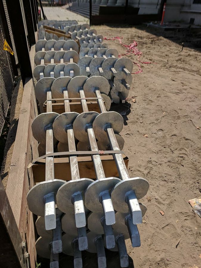 Rows of galvanized helical piles staged on site with their helix plates in view