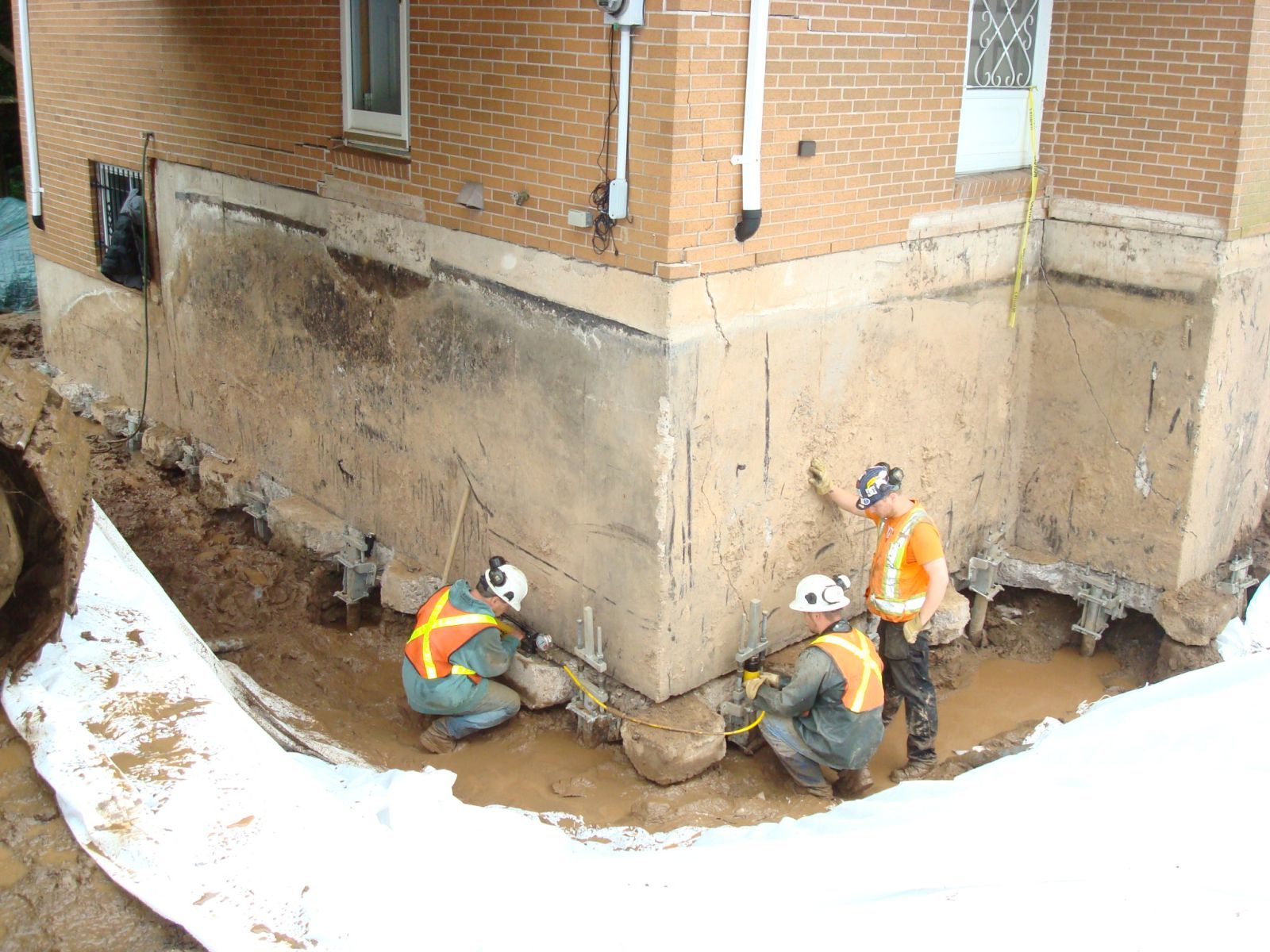 Crew working in an excavation along a brick foundation with support brackets installed