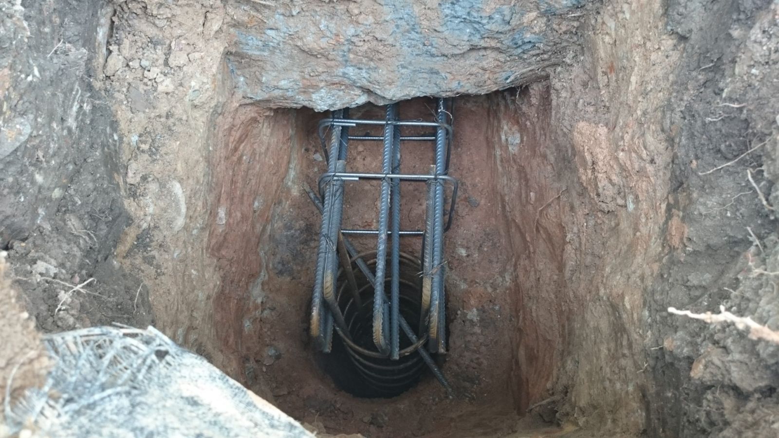 Foundation support bracket installed in an excavated pit beneath a wall