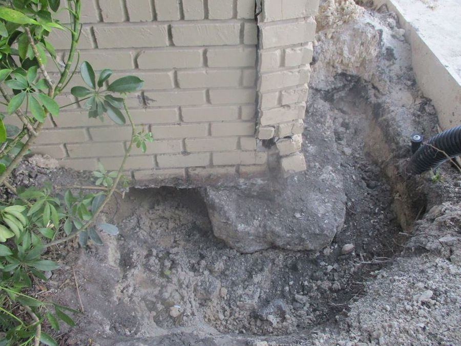 Concrete footing exposed at the corner of a brick foundation