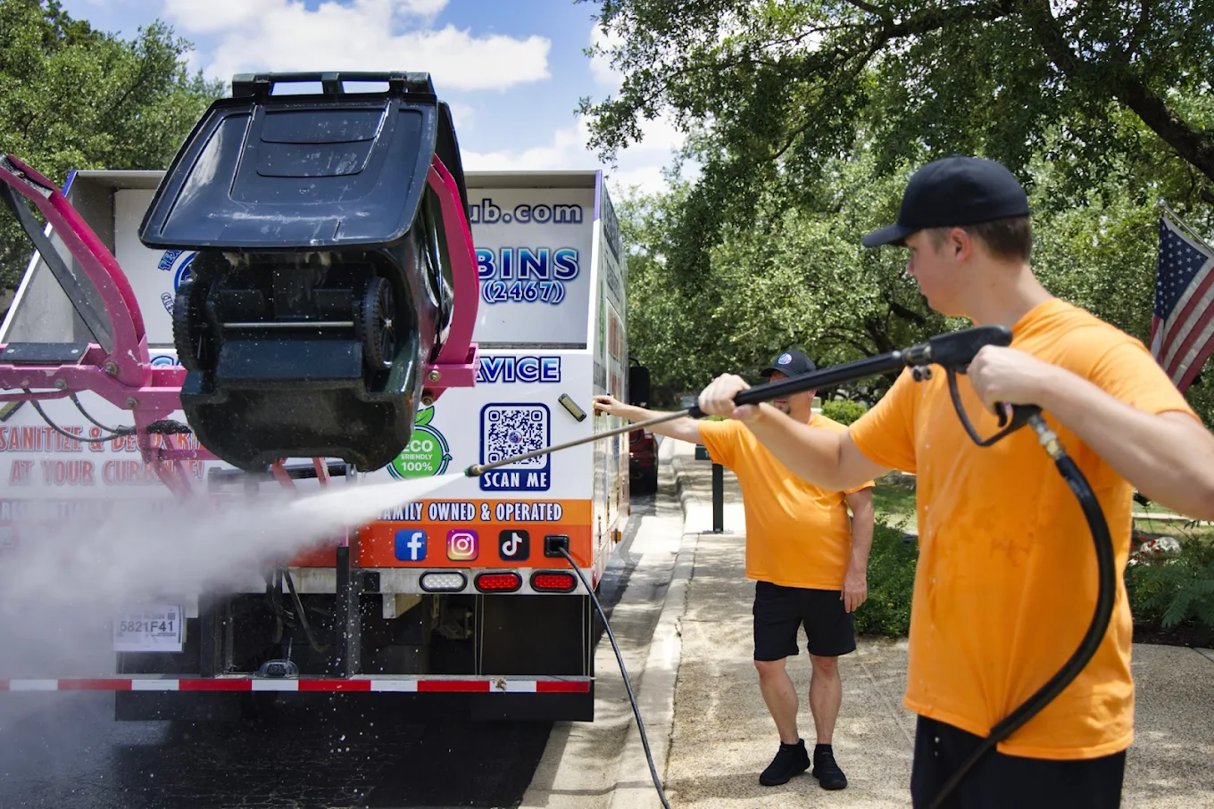 Trash bin cleaning service worker using high-pressure hot water to clean residential trash cans curbside in San Antonio.