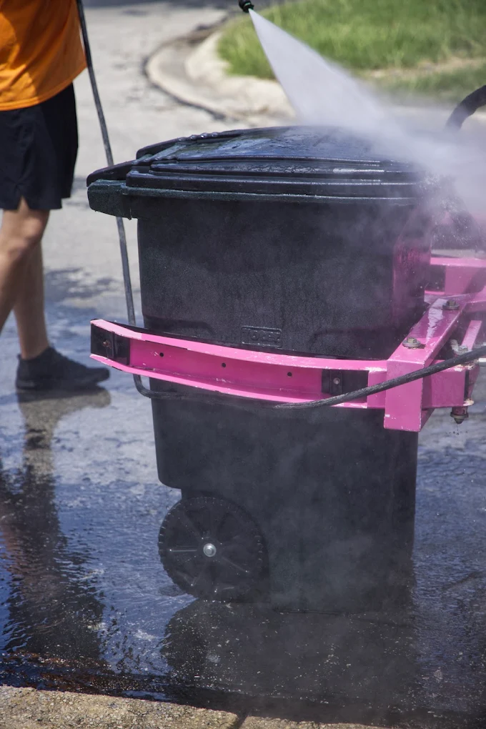 Trash bin cleaning service in San Antonio technician using high-pressure sanitizing equipment to clean residential trash cans.
