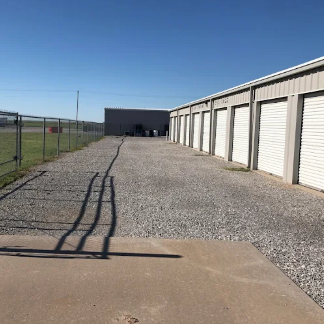 Drive-up storage units with white roll-up doors beside a gravel drive at the 37th Street location in Lawton, OK