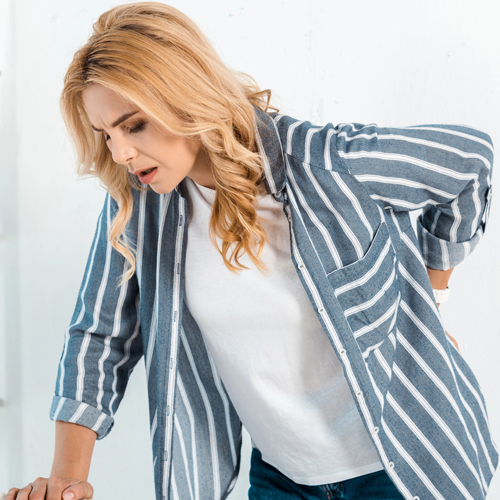 Woman clutching her lower back, indicating chronic back pain relief available through naturopathic therapies in Scottsdale.