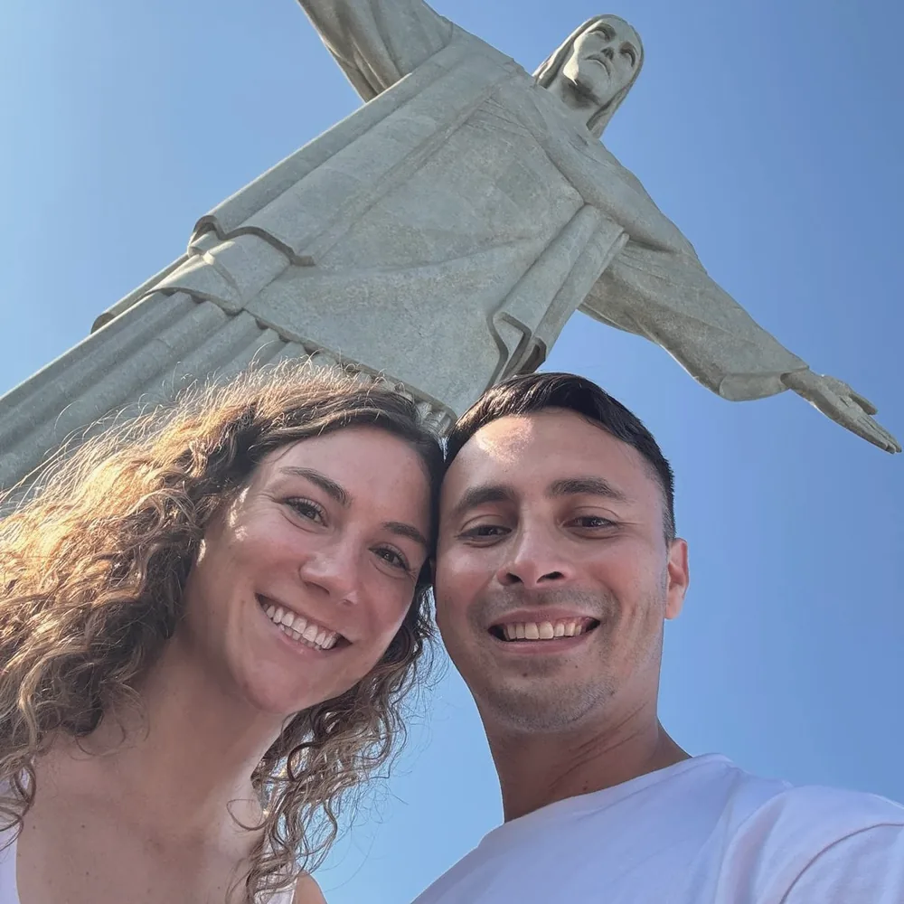 Elise and Ricardo smiling beneath Christ the Redeemer against a clear blue sky