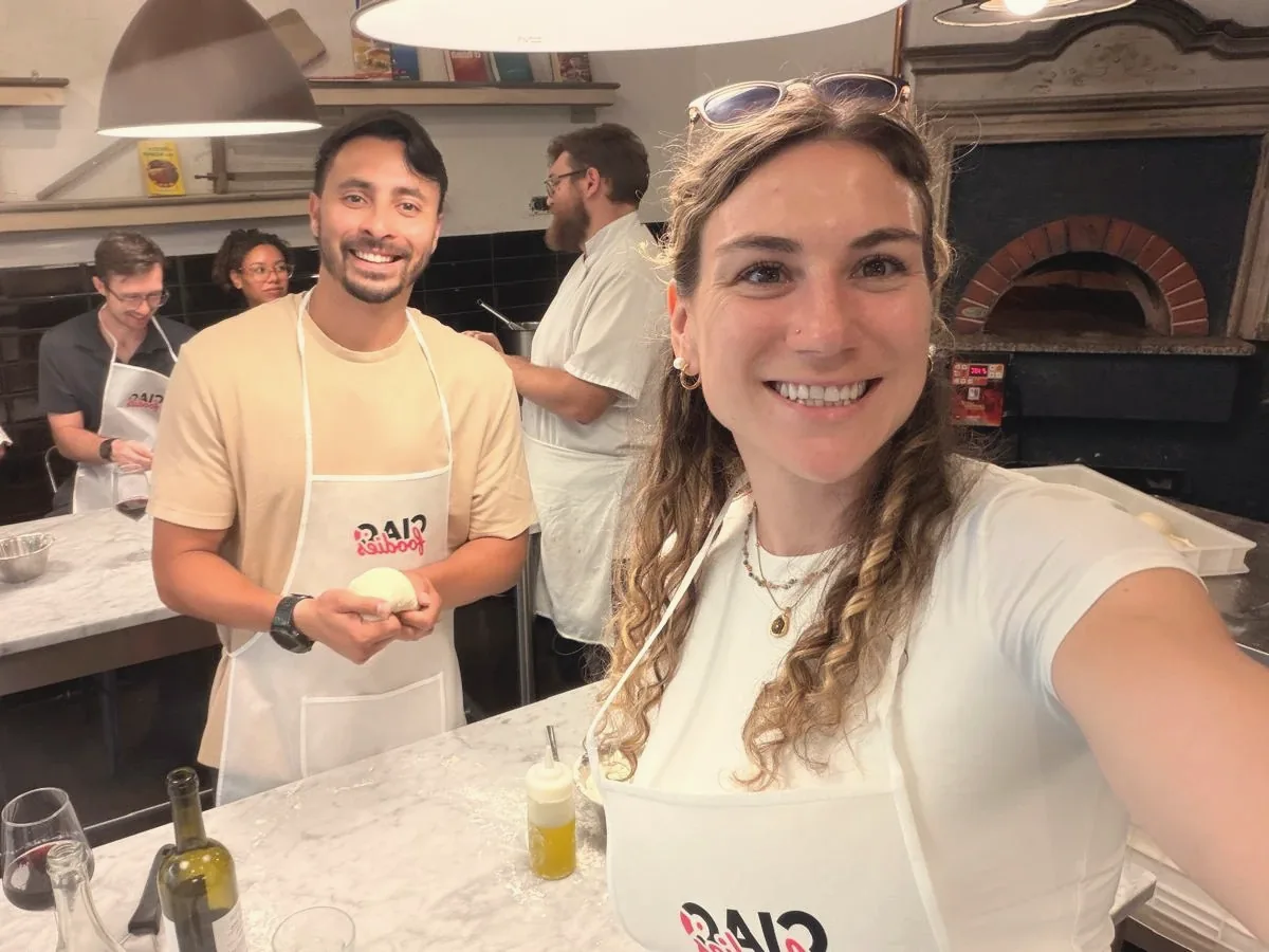 Elise and Ricardo in aprons at a pizza and gelato class in Italy, Ricardo holding a ball of dough